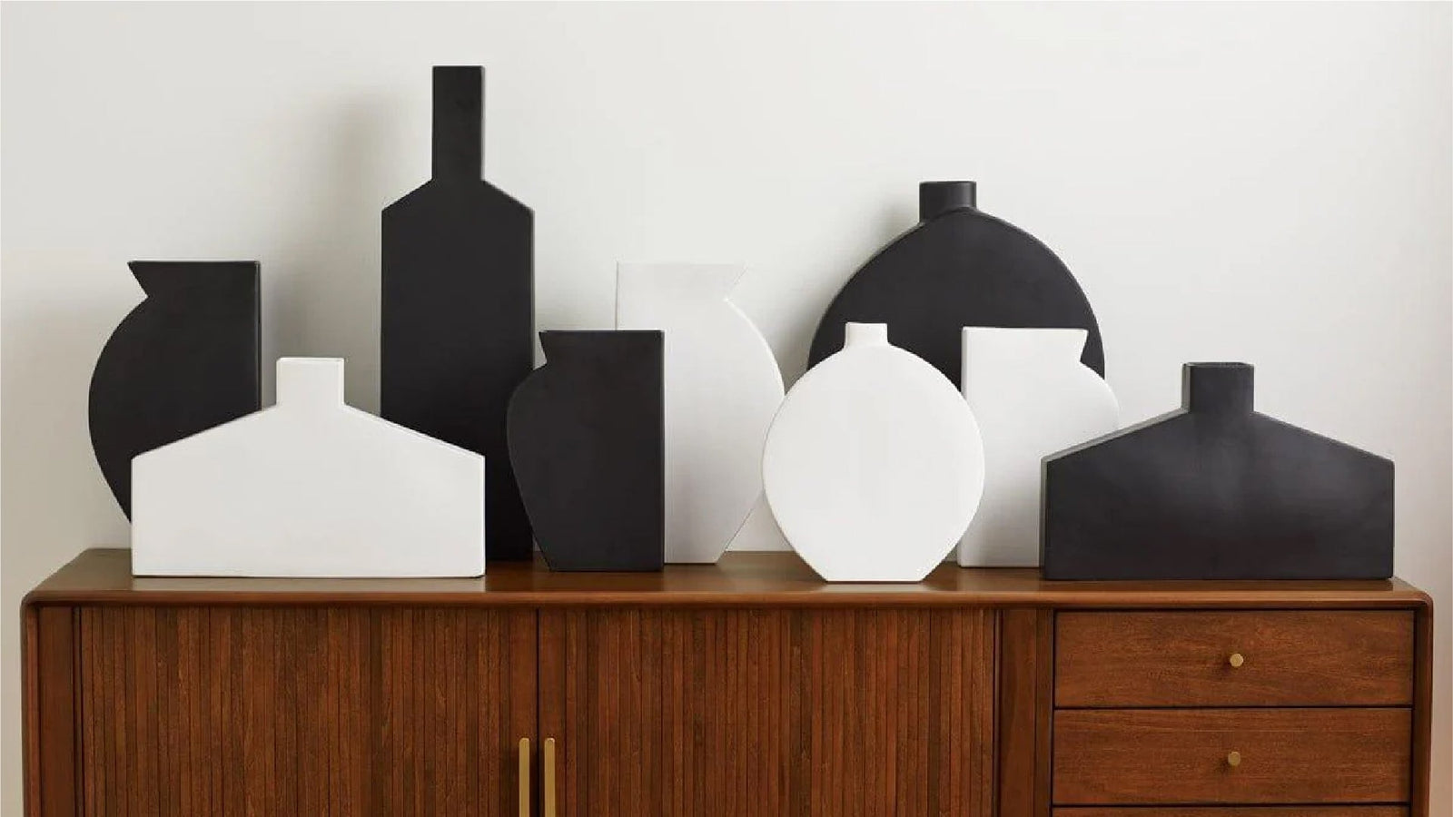 A collection of modern, geometric vases in black and white are arranged on a wooden sideboard. 