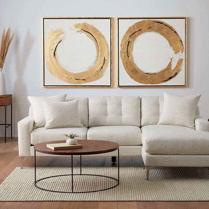 Modern living room with a beige sectional sofa, round wooden coffee table, and abstract wall art.